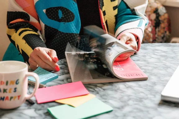 Eine Person liest eine Zeitschrift mit einem Becher auf dem Tisch, auf dem die Worte "DING KES HAPPY" stehen.